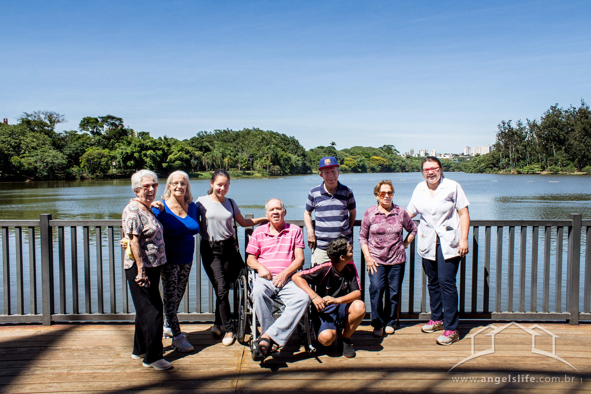 idosos apoiados em grade do deck do parque portugal em campinas, eles estao sorrindo para a foto juntamente com uma terapeuta ocupacional um motorista e uma acompanhante
